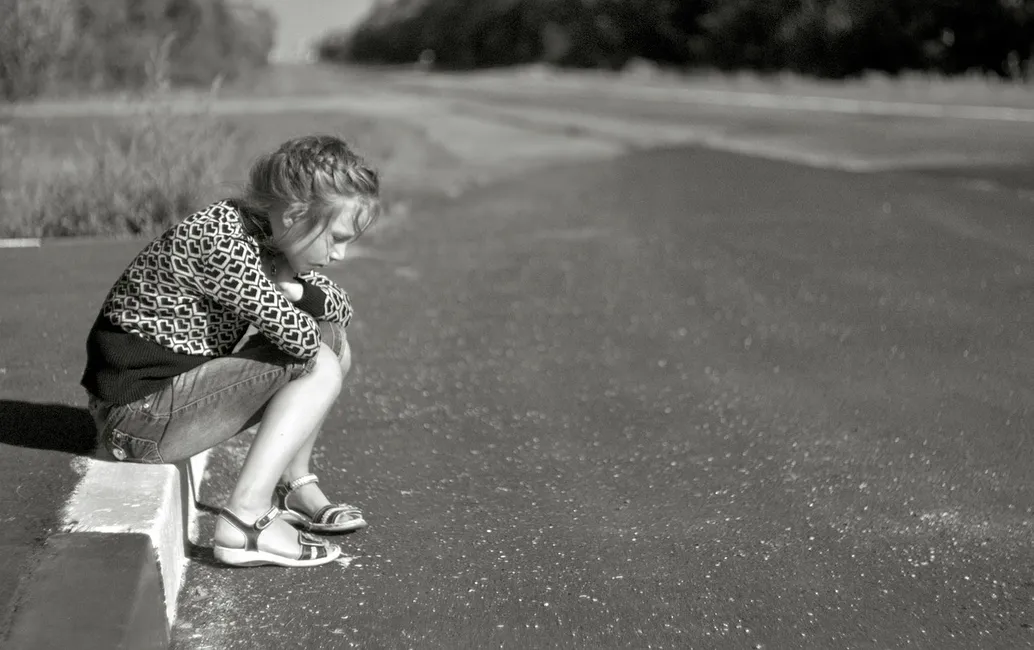 Lonely girl sitting on curb.