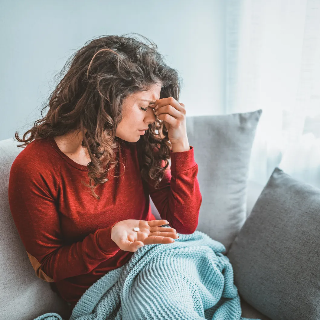 Young women sitting on the couch holding her head due to a headache. 