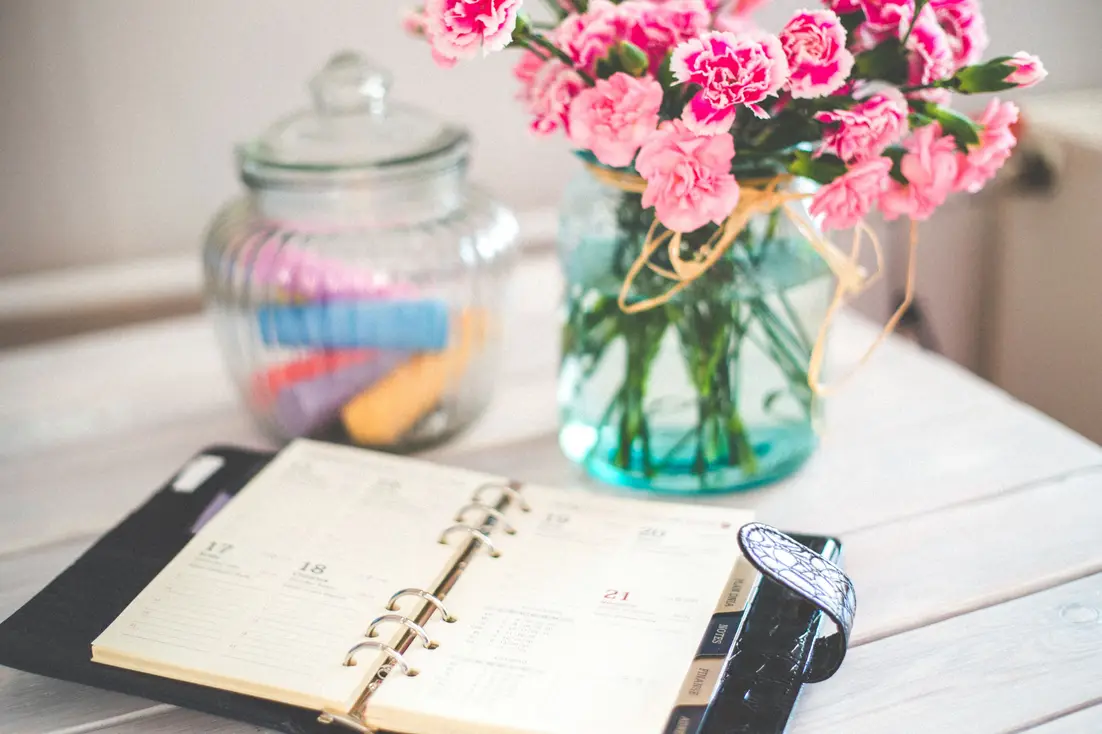 open planner on a desk with a jar of chalk and a vase of flowers