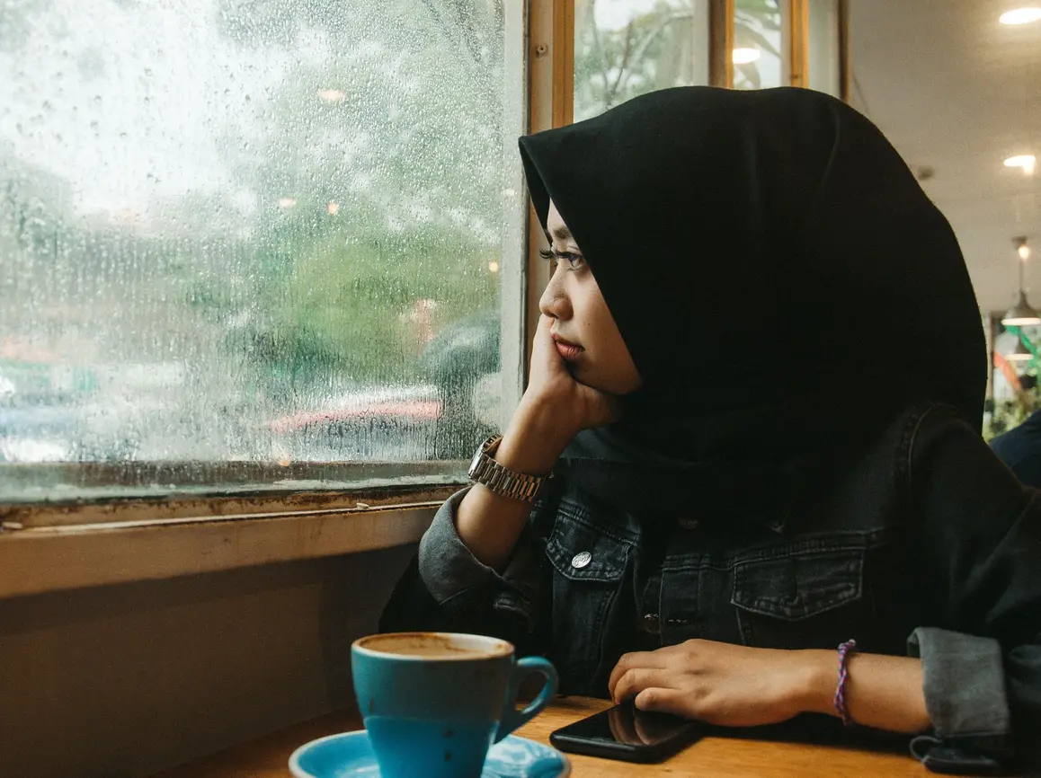 young woman looking out rainy window