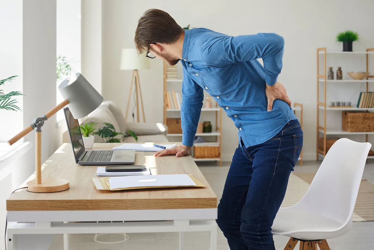Man standing up at his desk and his hand on his lower back