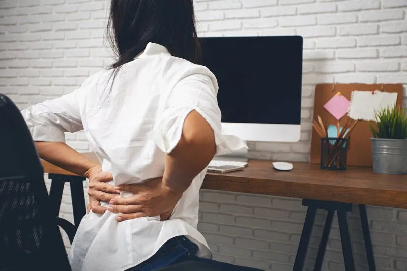 woman at desk holding sore back