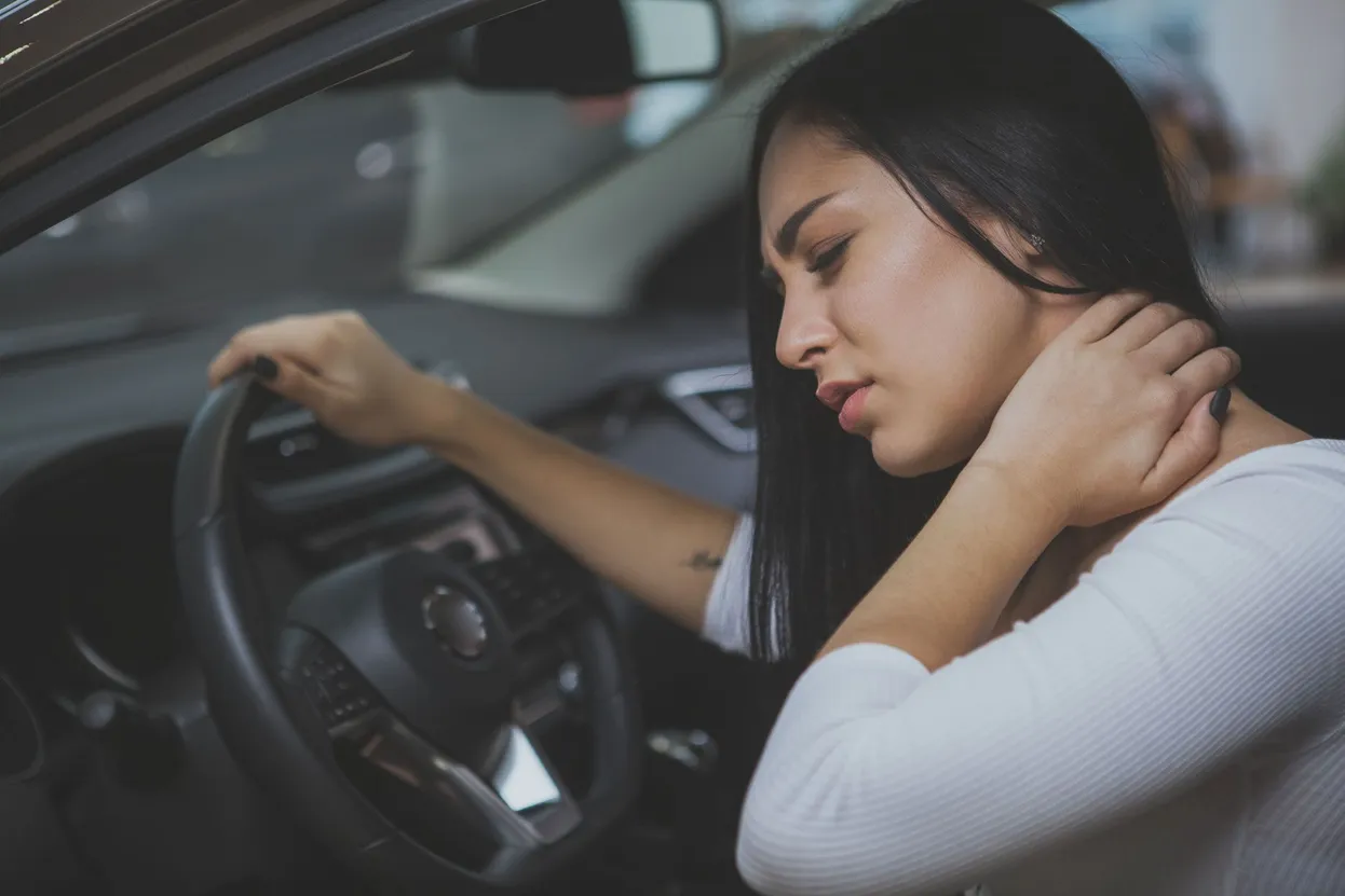 woman sittin in her car following a car accident holding her neck