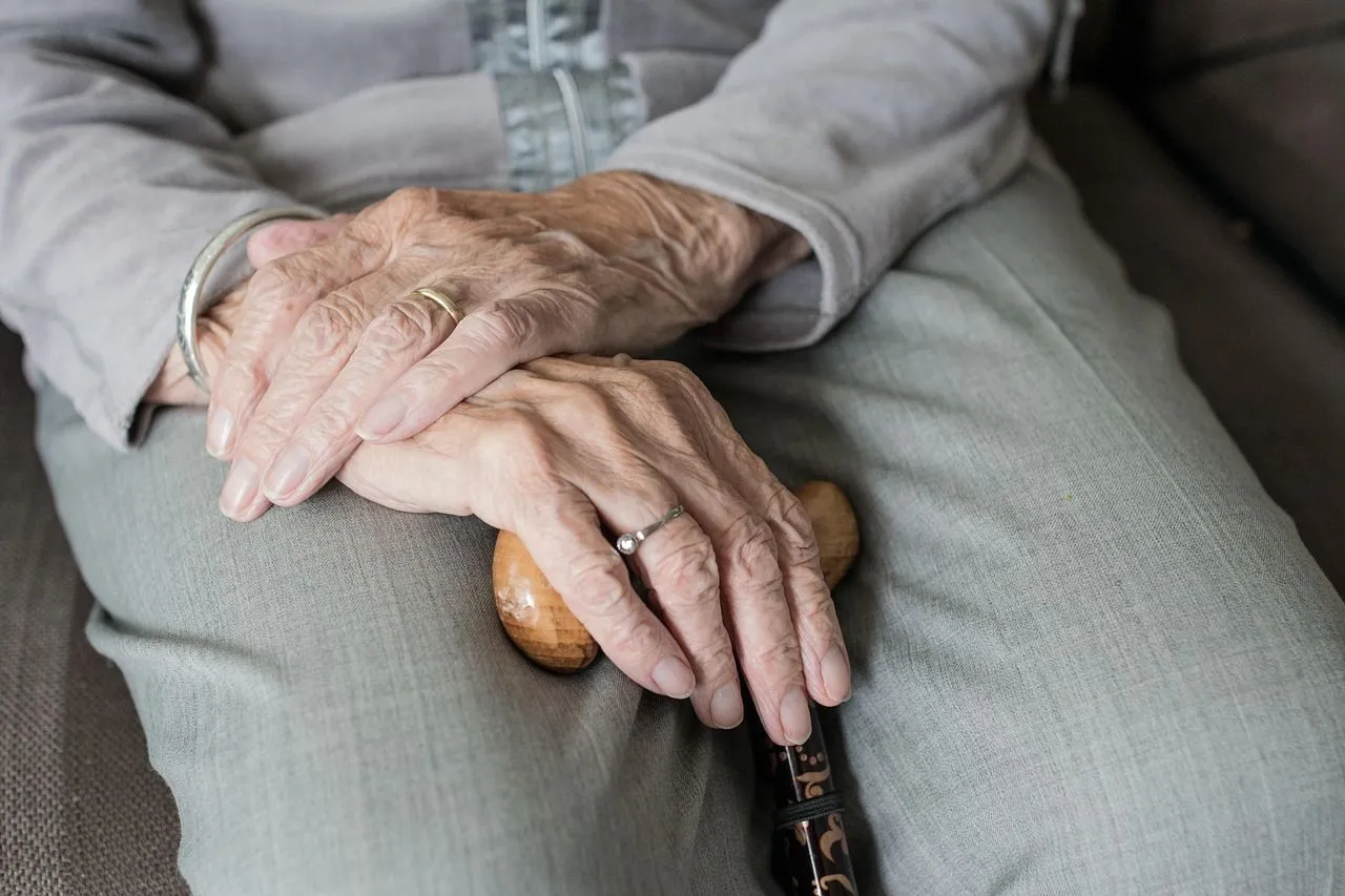 older woman sitting in chair holding a cane with her hands placed over each other