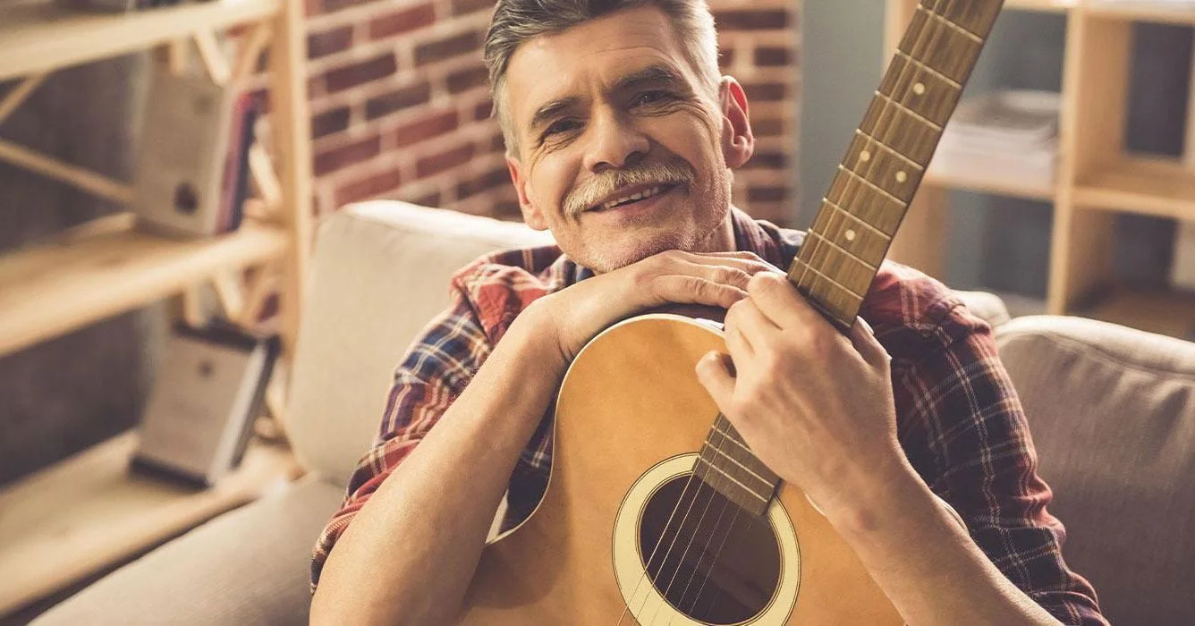 Man Sitting With Guitar And Smiling