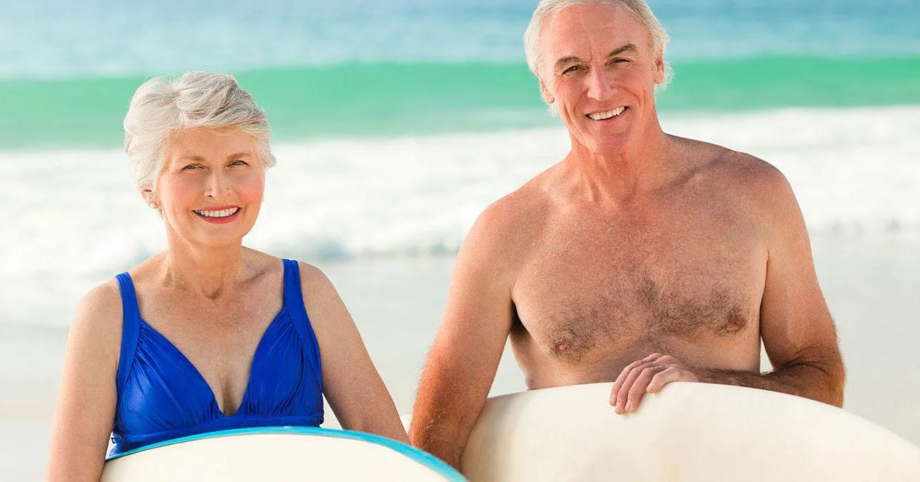 Elderly Couple Holding Surfboards At The Beach