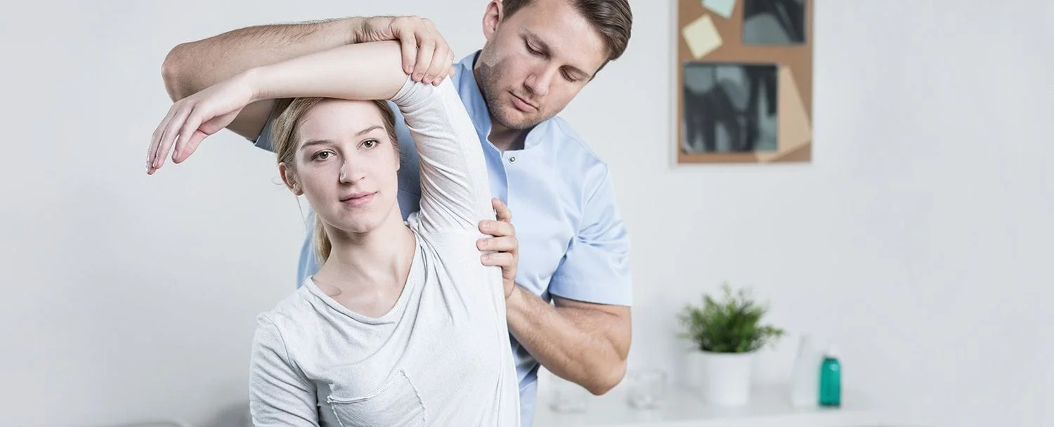chiropractor adjusting a woman's shoulders during corrective exercises for physical therapy