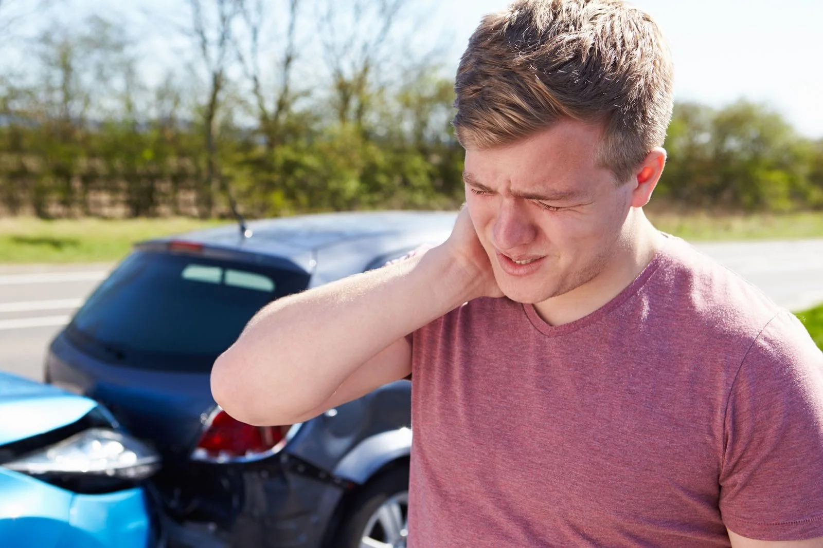 man holding his neck from whiplash pain from an auto accident injury; car accident in the background