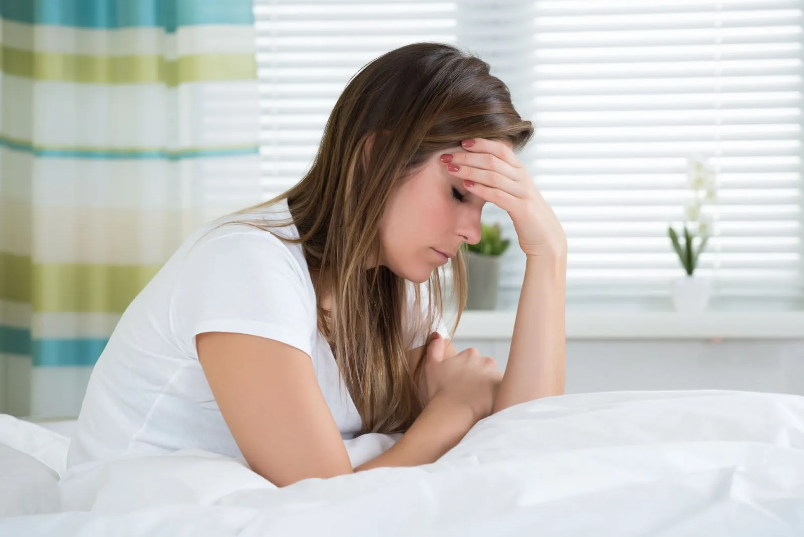 woman in bed holding her forehead in pain from a migraine