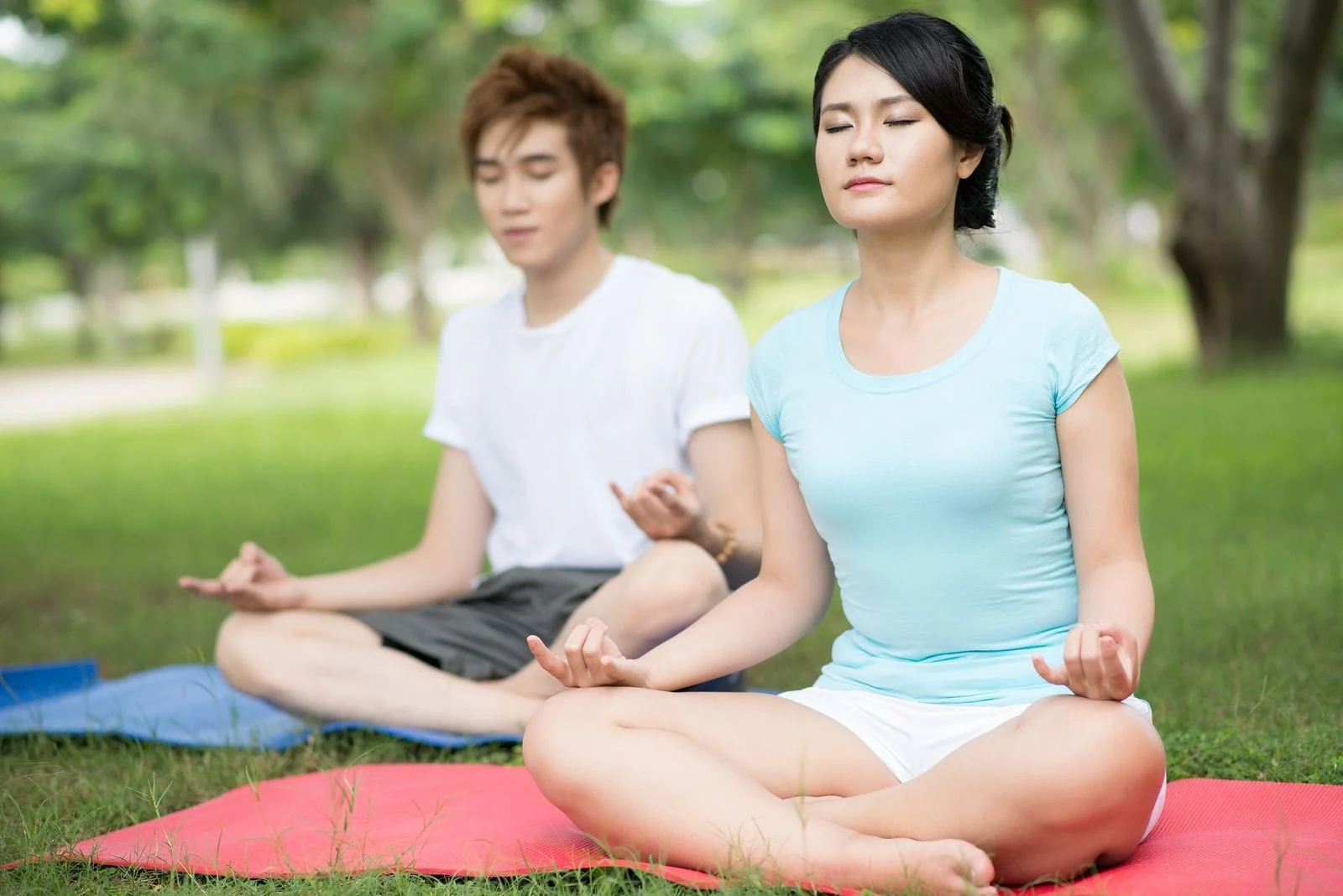 Young Asian man and woman outdoors in lotus position seated on yoga mats on the grass
