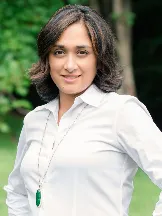 Picture of Vinaya Saunders smiling and wearing a white blouse against a background of green foliage in the woods