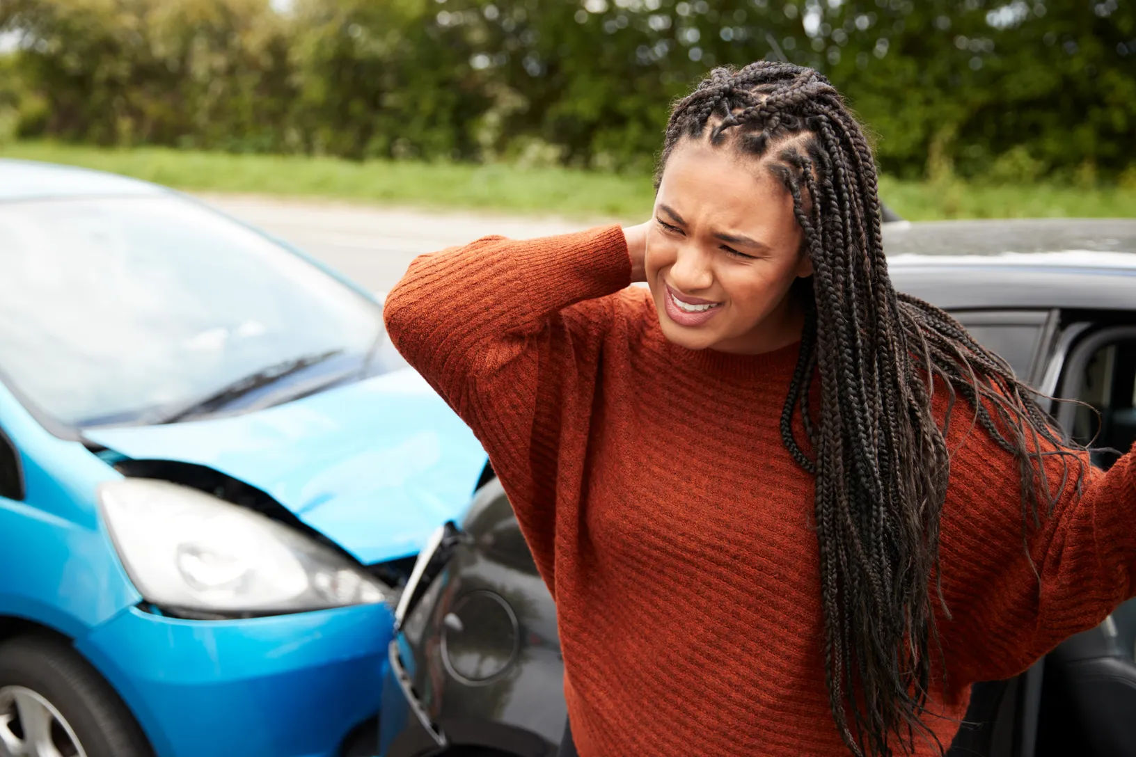 Auto accident photo. Women with neck injury with can accident behind her. 