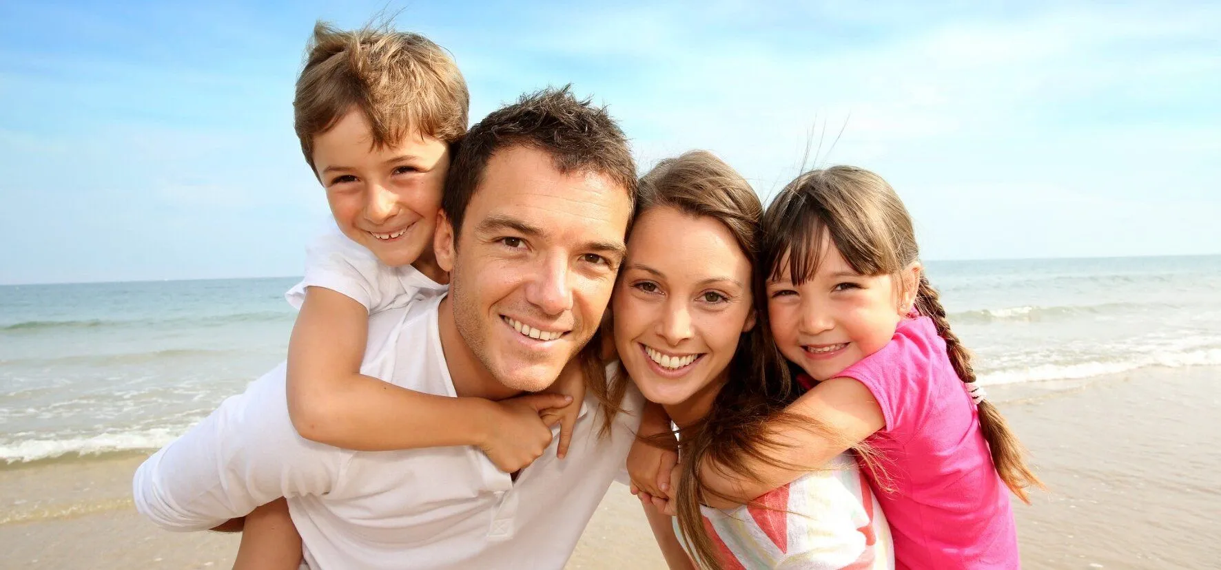 mom and dad holding boy and girl on beach, smiling, restorative dentistry Millbrae, CA dentist