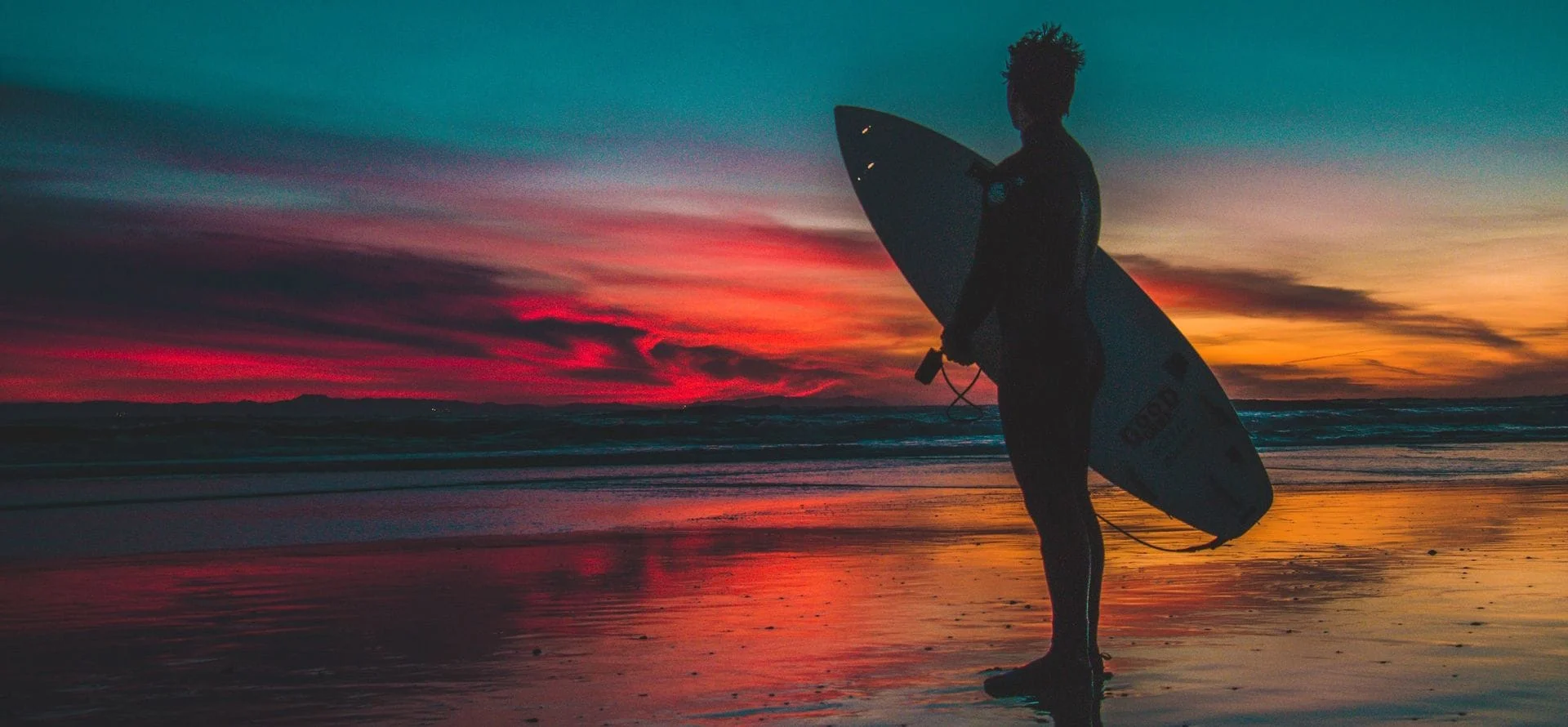 Image of a surfer standing by the ocean when the sun is about to set.