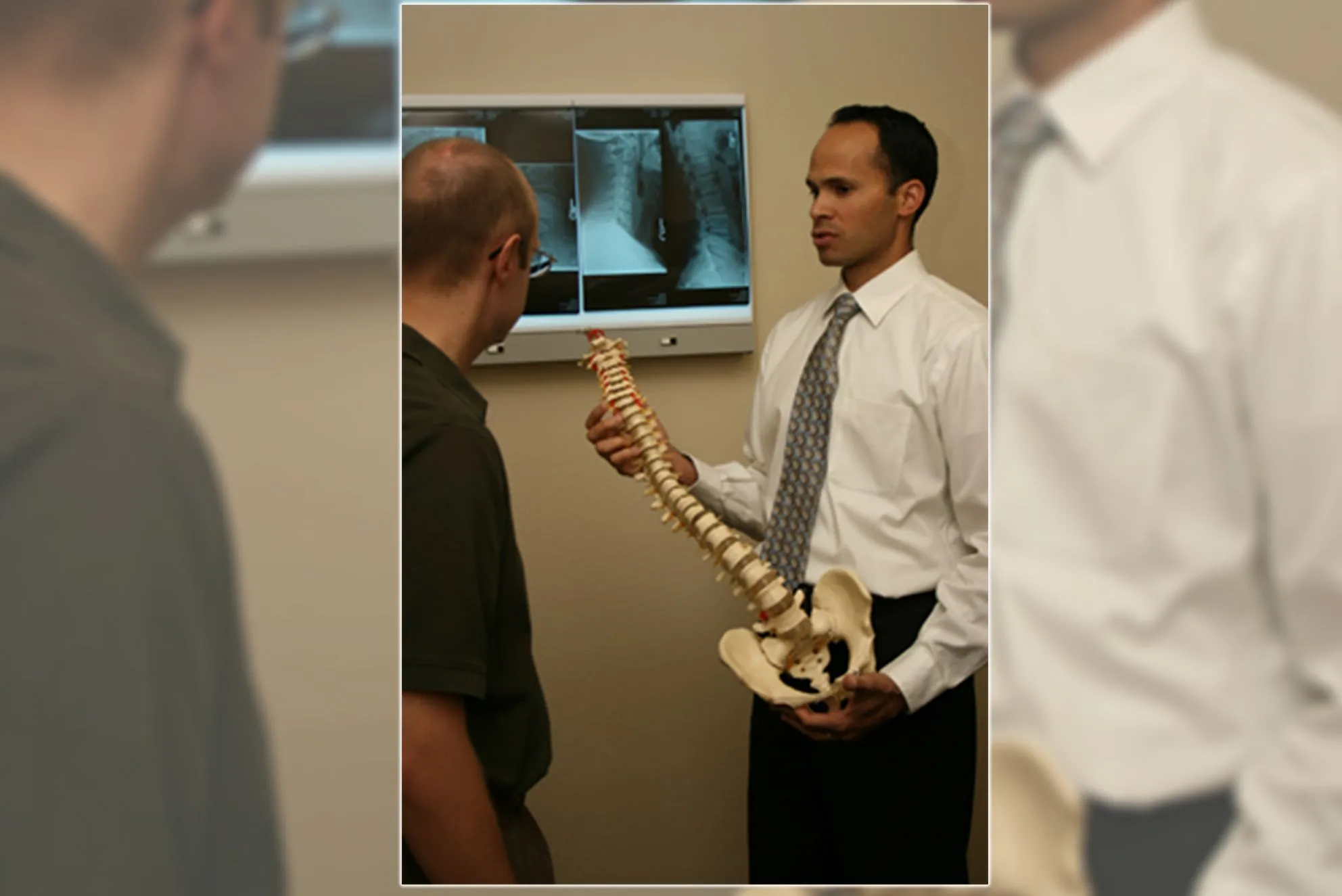 Dr. Yamamoto holding a model of a spinal cord talking to a patient