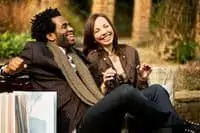 African american man and caucasian woman smiling and sitting on bench
