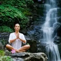 woman meditating near waterfall