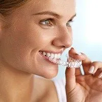 woman smiling looking right, hand holding clear aligner tray near mouth, Invisalign Melrose, MA orthodontics