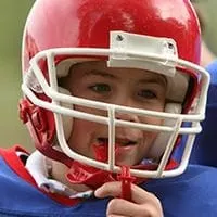young boy wearing football helmet putting mouthguard in mouth, custom sports mouthguards Melrose dentist
