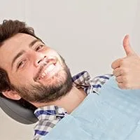 man lying back in dental chair wearing dental bib, smiling and giving thumbs up, family dentistry Melrose, MA