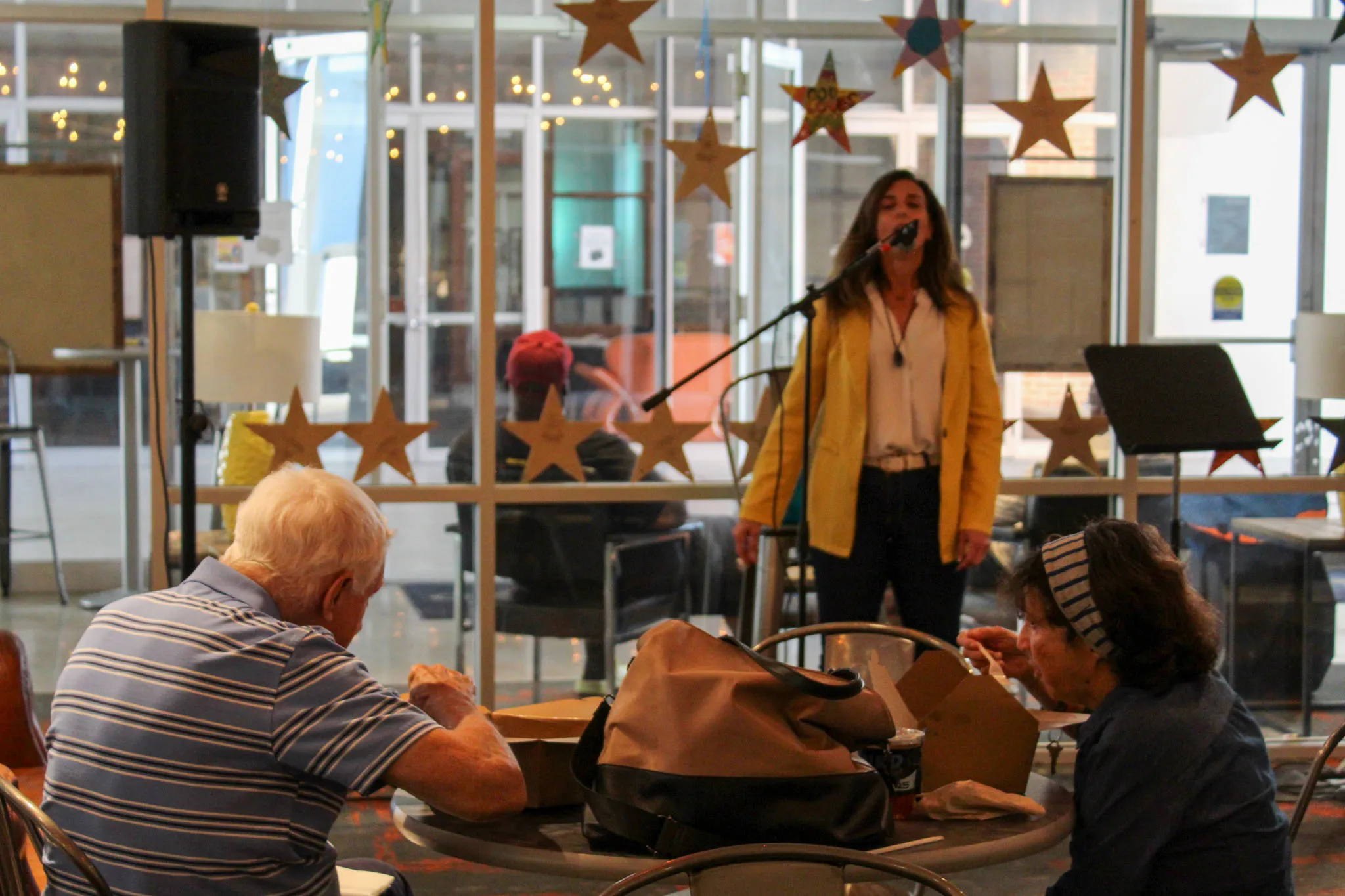 a woman singing and people sitting at a table conversing in front of the singer