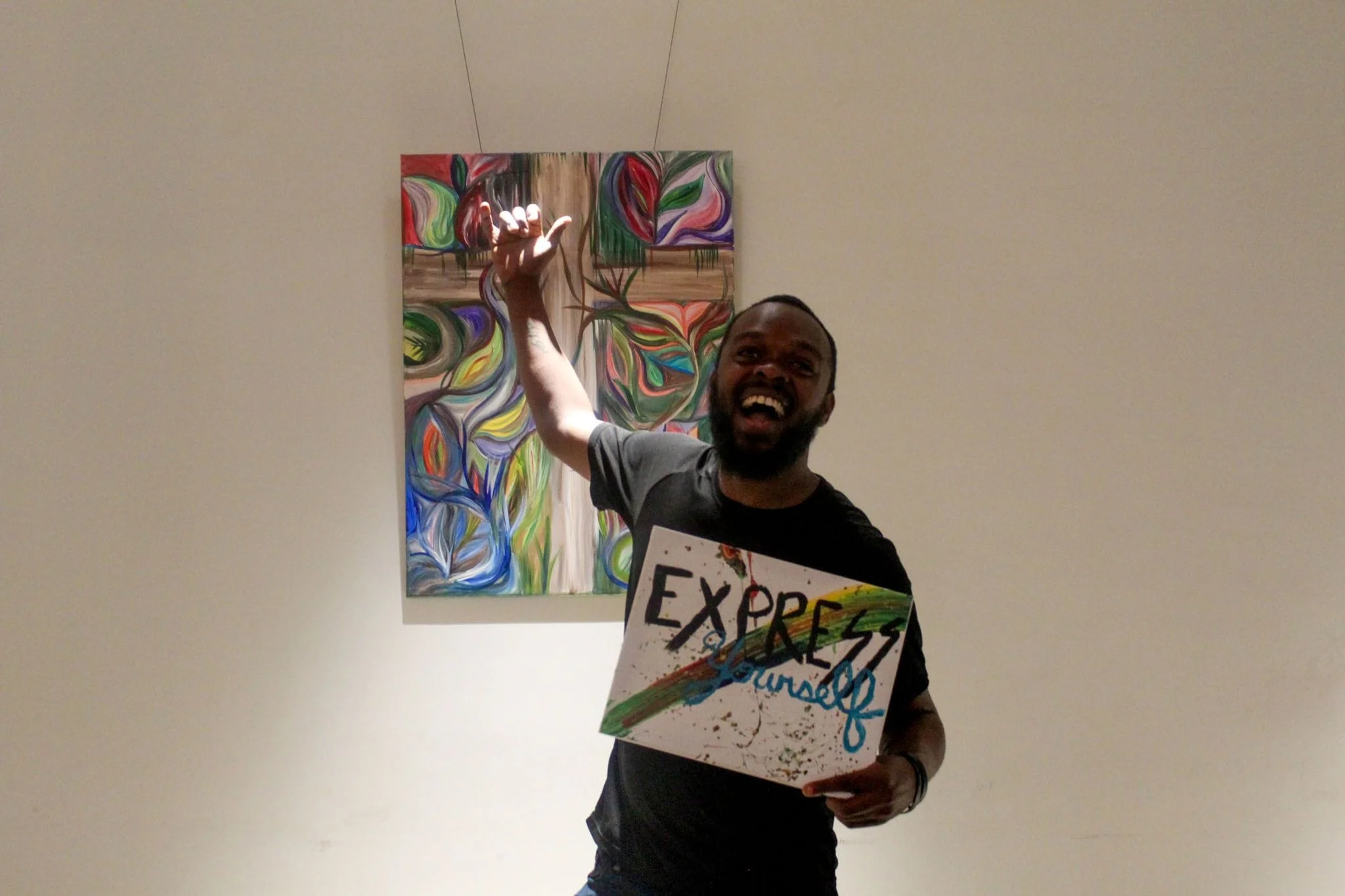 a man smiling in front of a painting, holding his own painting that reads "Express yourself"