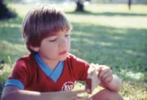 young boy eating a sandwich in a park