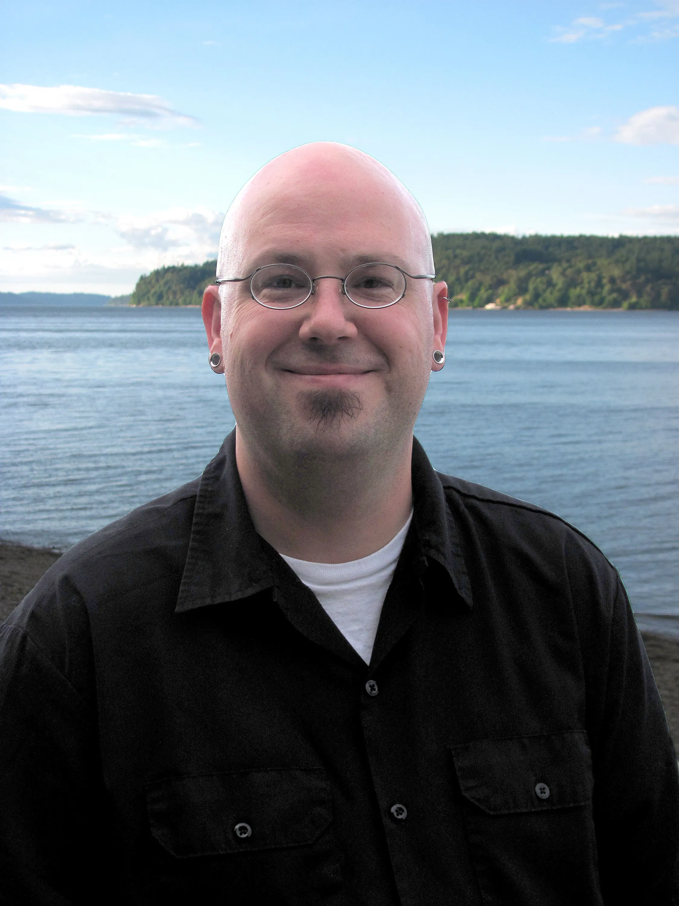 Ron stands in front of a green coastline, smiling.