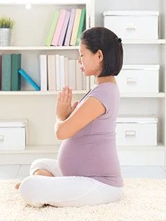 Pregnant woman in seated yoga pose with hands together in front of her heart