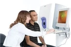 A young man and woman, next to an eye exam machine, looking at the Optomap Retinal eye exam.