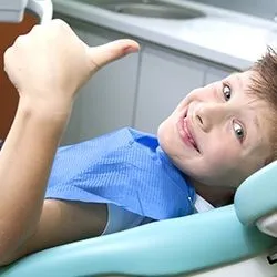 Young boy in dental chair giving thumbs up 