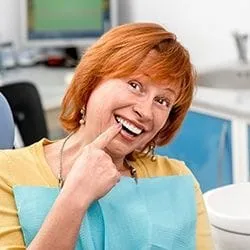 Senior woman in dental chair pointing to flawless smile
