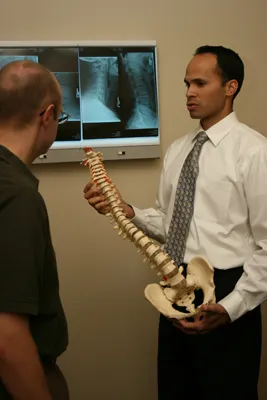 Dr. Yamamoto holding a model of a spinal cord talking to a patient