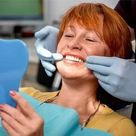 dentist hands by older red haired woman's mouth, woman looking in mirror at teeth, dental implants Albuquerque, NM
