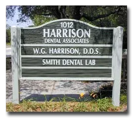 Green wooden sign for Harrison Dental Associates, cosmetic dentist office in Panama City, FL