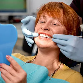 dentist's hands on red haired older woman's mouth, showing her teeth in mirror, dental bridge Longmont, CO