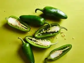 Green jalepeno peppers cut in halves with seeds showing on a lime green background