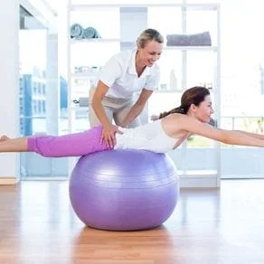 A chiropractor helps her patient exercise on an exercise ball