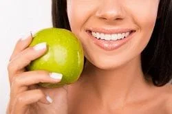 Woman holding an apple next to her perfect smile after seeing her cosmetic dentist in Panama City, FL