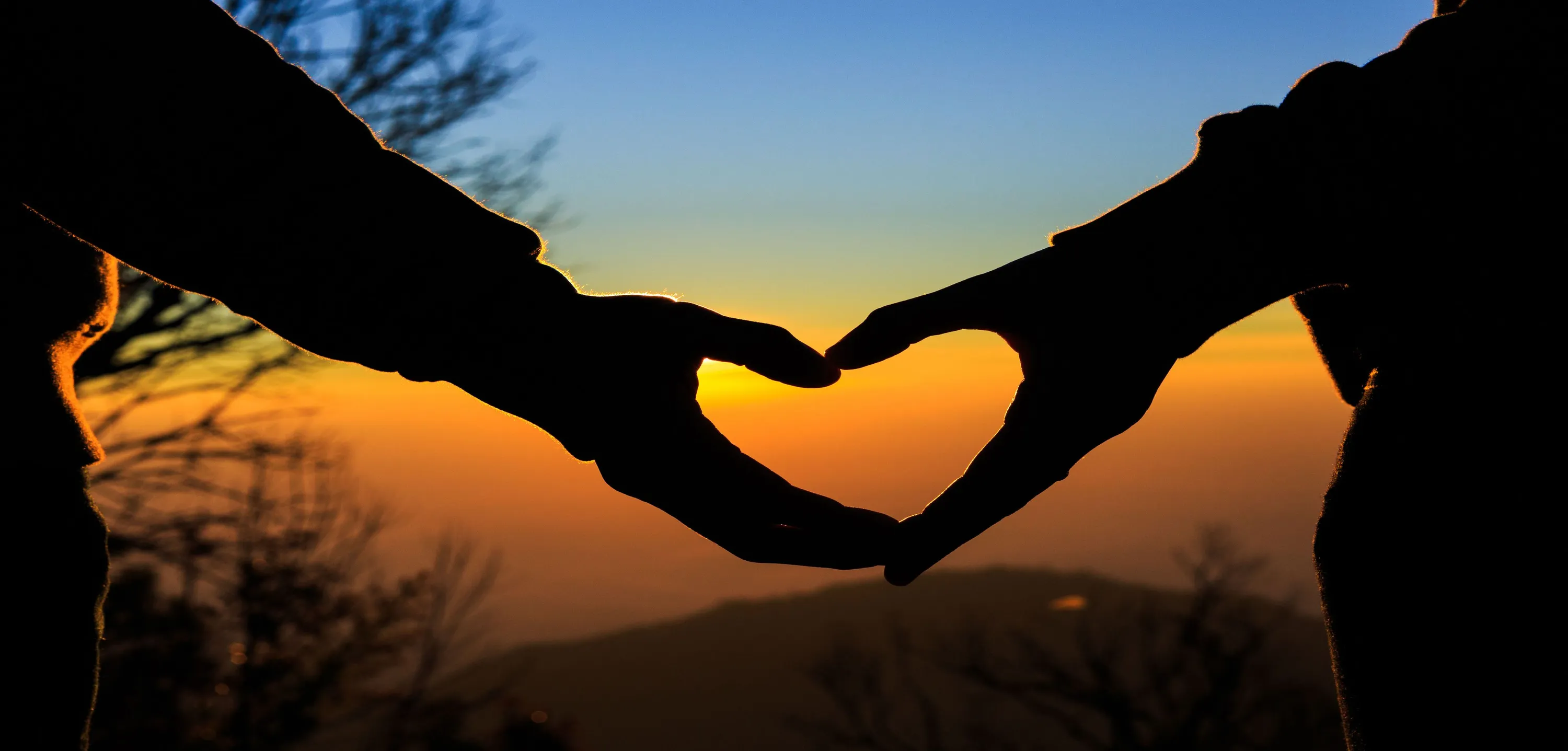 Silhouette of a couple making a heart with a sunset in the background.