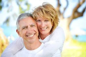 older couple smiling near trees and water, dental implants Annapolis, MD