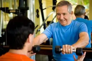 younger man helping elderly man in gym