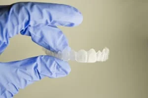 blue gloved hand holding clear teeth aligner, Invisalign clear braces Millbrae, CA dentist