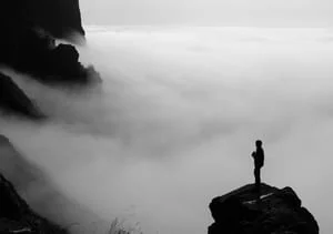figure alone on a cliff above the clouds