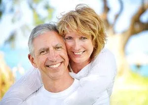 mature couple smiling outdoors near water and trees, San Jose, CA dental implants