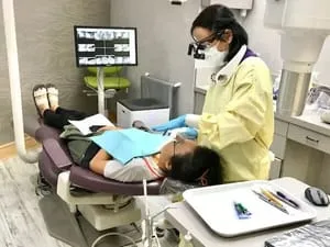 female dental assistant cleaning patients teeth, X-ray image in background on computer, teeth cleaning Millbrae, CA dentist
