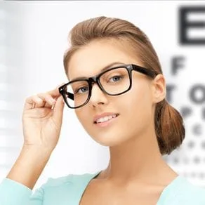 A head shot of young woman with glasses posing against the background of a Snellen chart