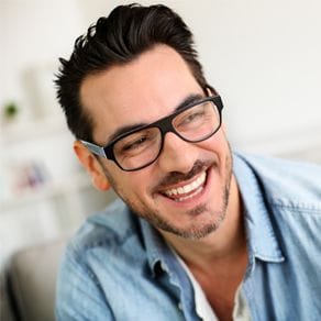 A man with glasses dressed in a jeans jacket smiling