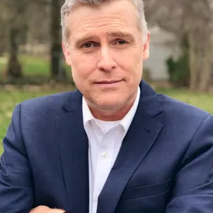 middle aged man with folded arms in front of trees