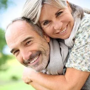 Man giving woman piggyback ride, both smiling with dental implants in North Little Rock, AR
